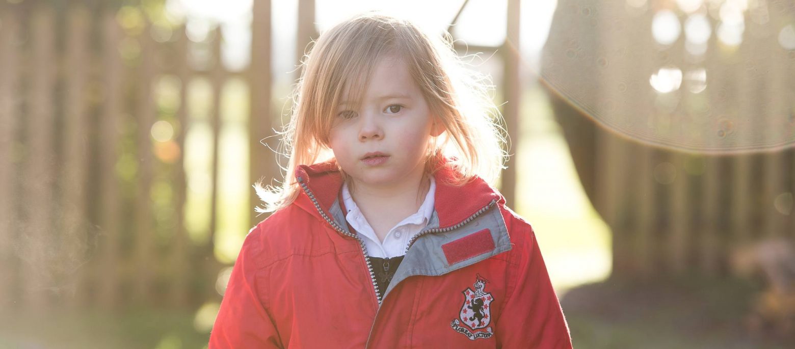 A school girl looking at the camera as the sun makes a glint on the camera