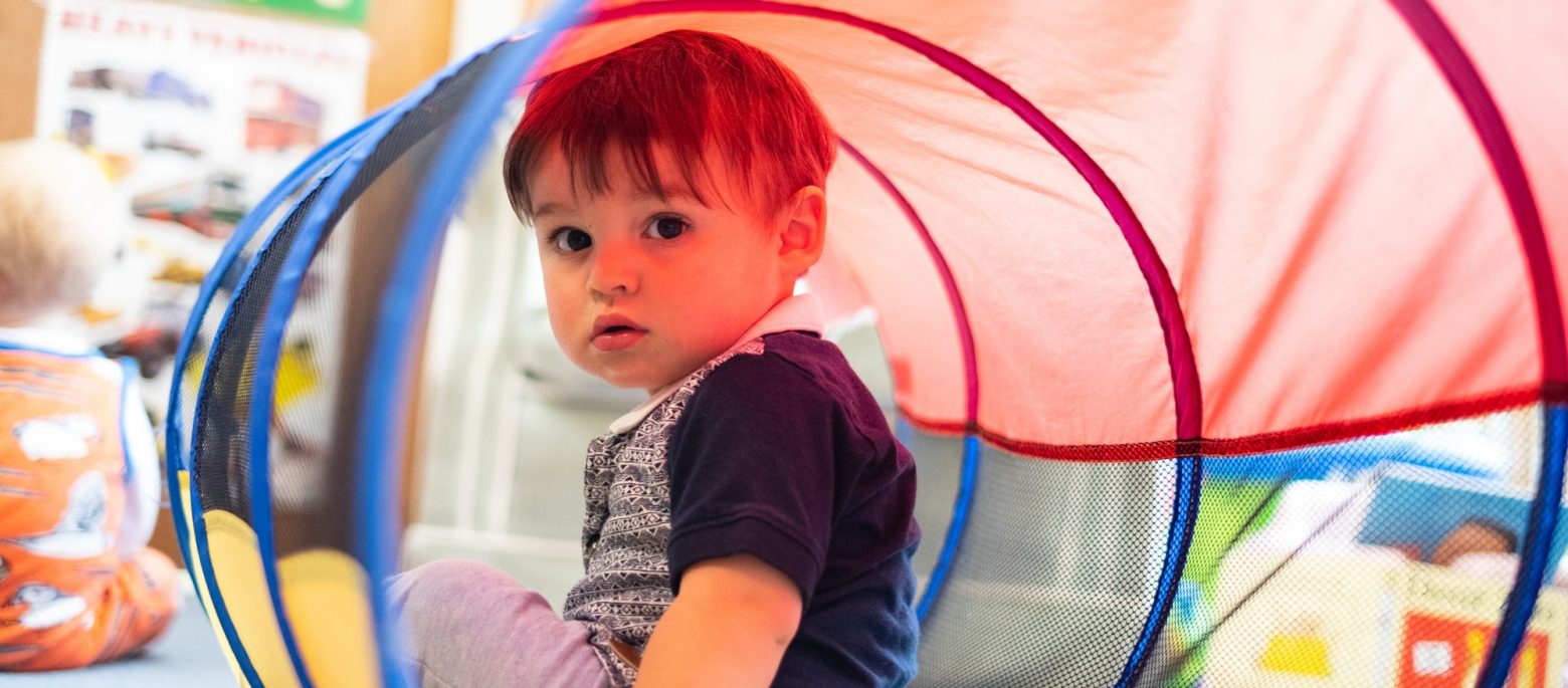 A young boy in a plastic tunnel as they're enjoying play time