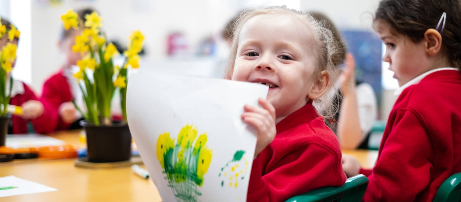 A smiling girl holding up a painting she's done of some daffodils