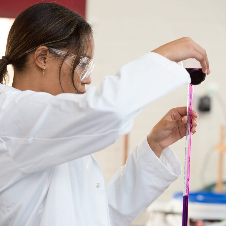 Student pouring purple liquid into long test tube