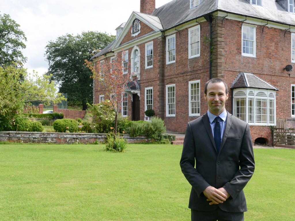 One of the school teachers smiling in front of the Lucton School building and grounds