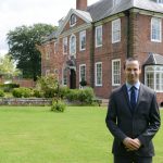 One of the school teachers smiling in front of the Lucton School building and grounds